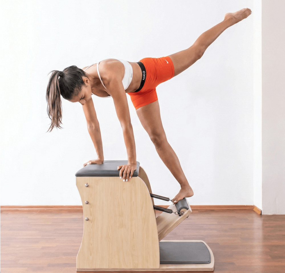 woman performs a Pilates exercise on a light wood Wunda Chair.